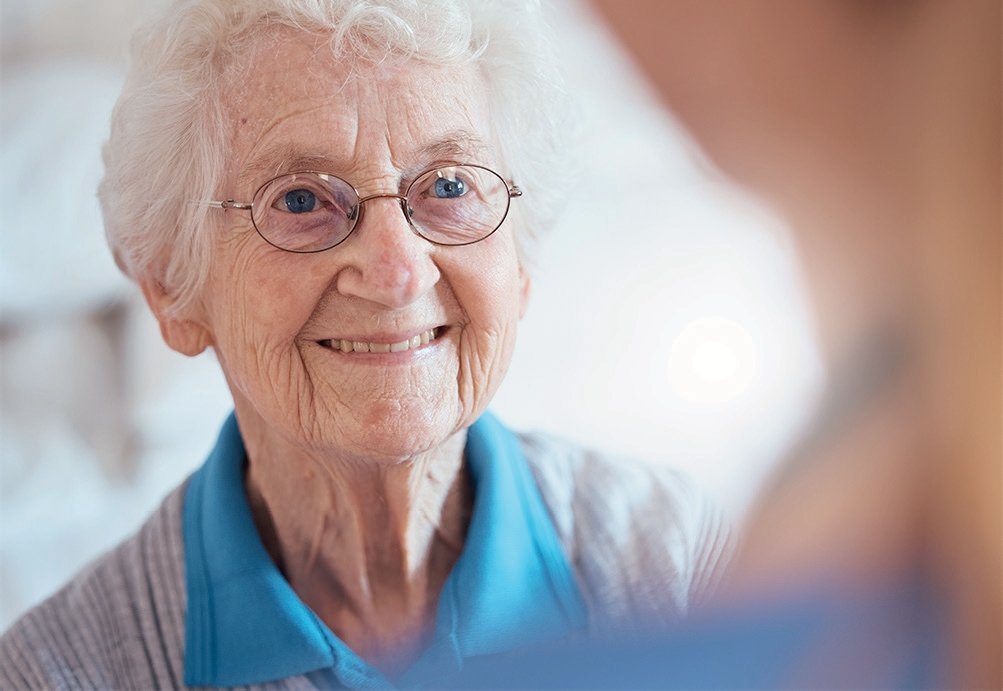 Idosa sorridente de cabelos brancos e óculos redondos na residência sénior em Sintra